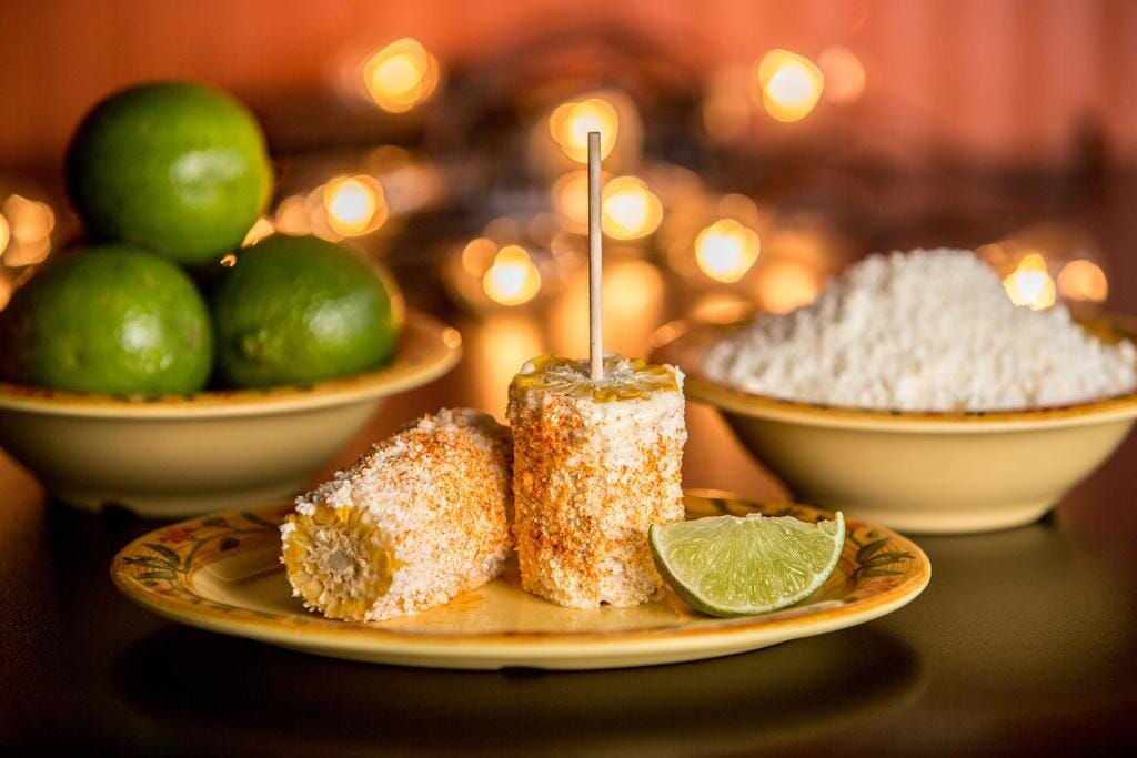 Seasoned corn covered in white sauce next to a lime on a plate